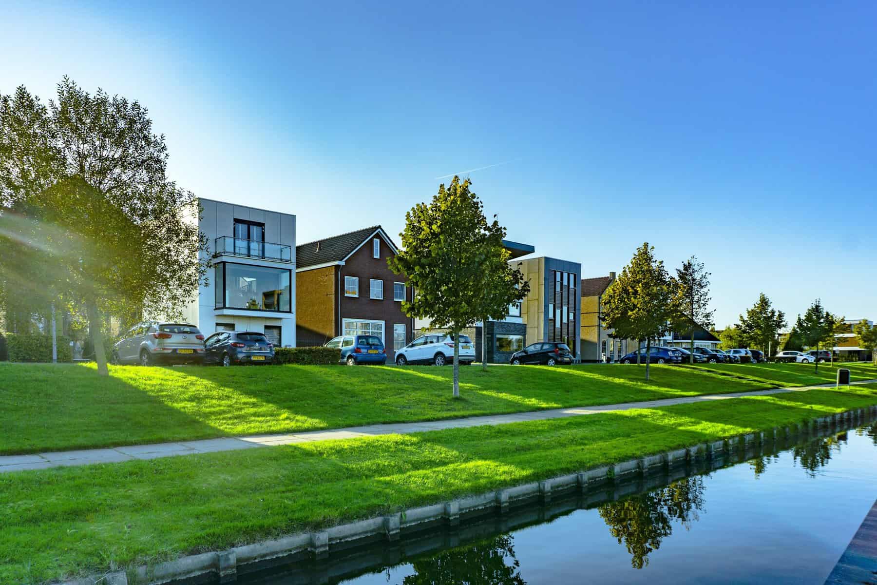 Row of houses on a grassy length that runs parallel with a water front.